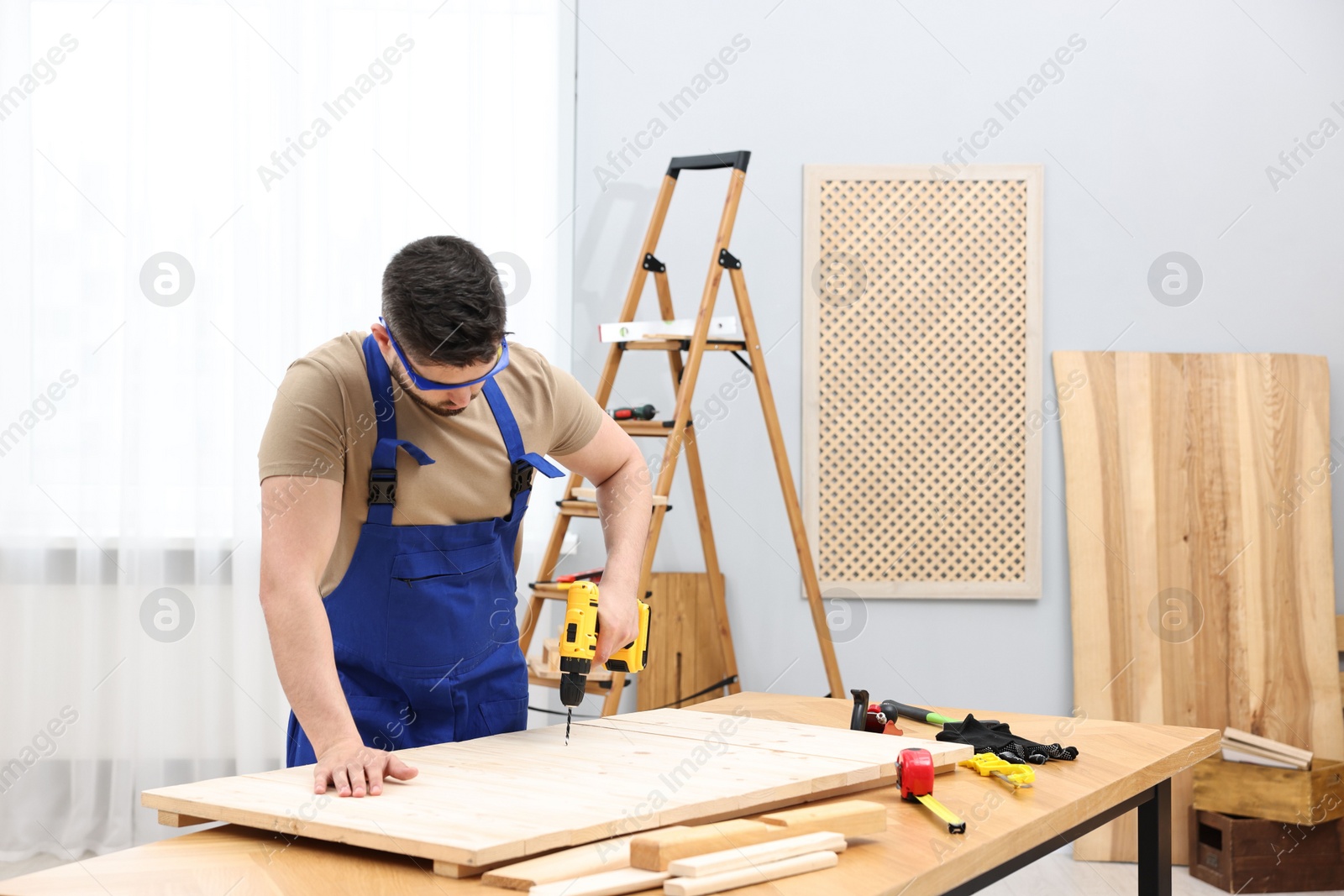 Photo of Young worker using electric drill at table in workshop