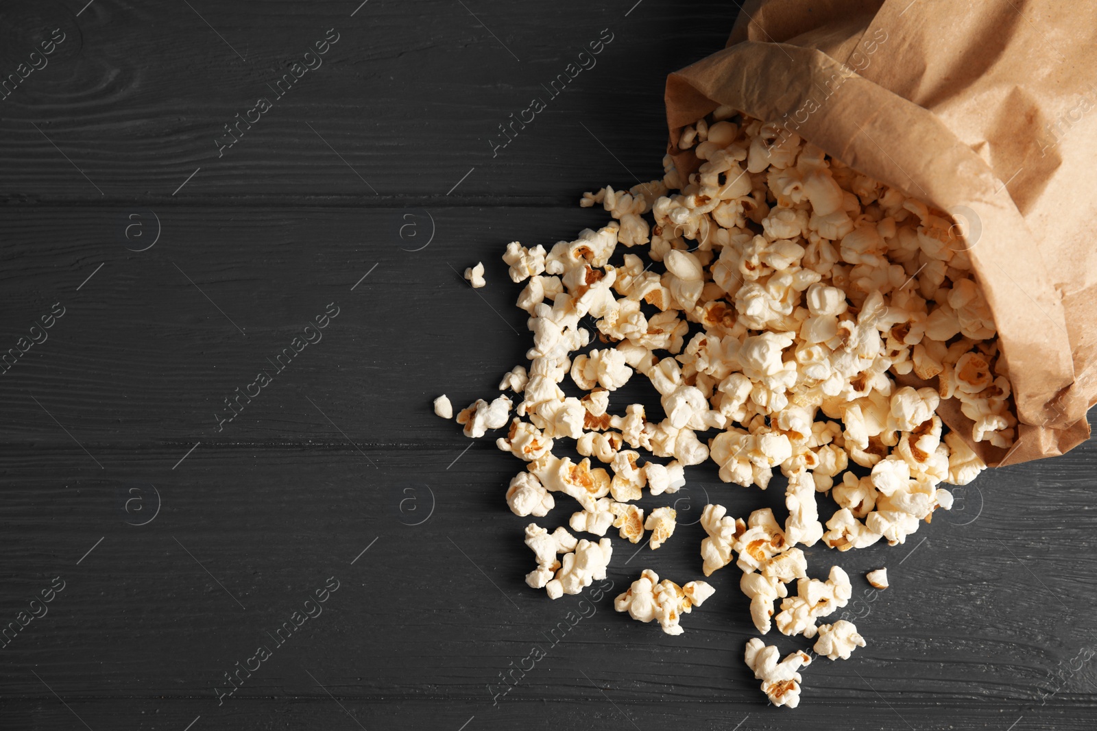 Photo of Paper bag with tasty popcorn on wooden background