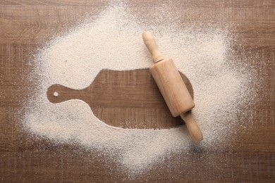 Photo of Imprint of board on wooden table with flour and rolling pin, top view