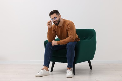 Photo of Handsome man sitting in armchair near white wall indoors