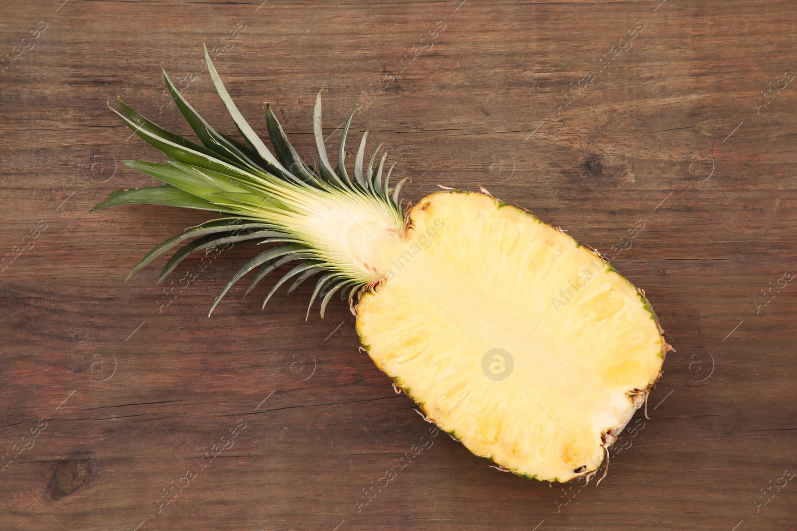 Photo of Half of ripe pineapple on wooden table, top view