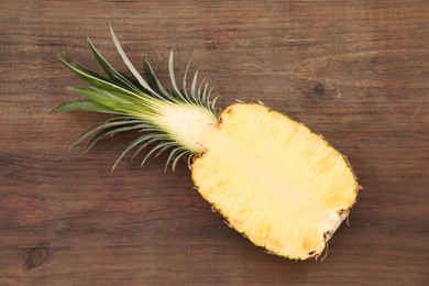Photo of Half of ripe pineapple on wooden table, top view