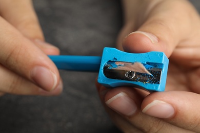 Photo of Woman sharpening pencil at grey table, closeup