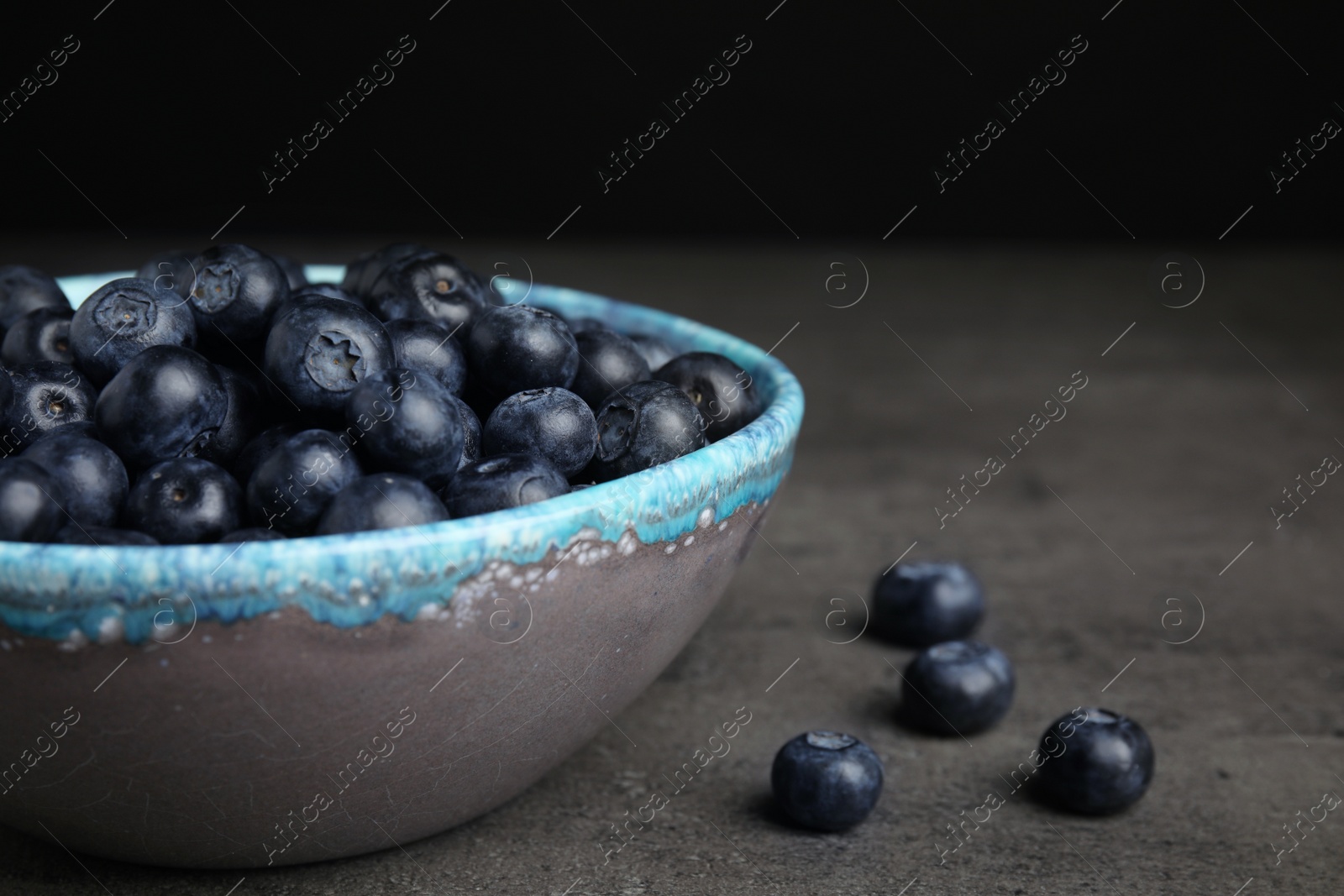 Photo of Bowl of tasty blueberries on grey table, space for text