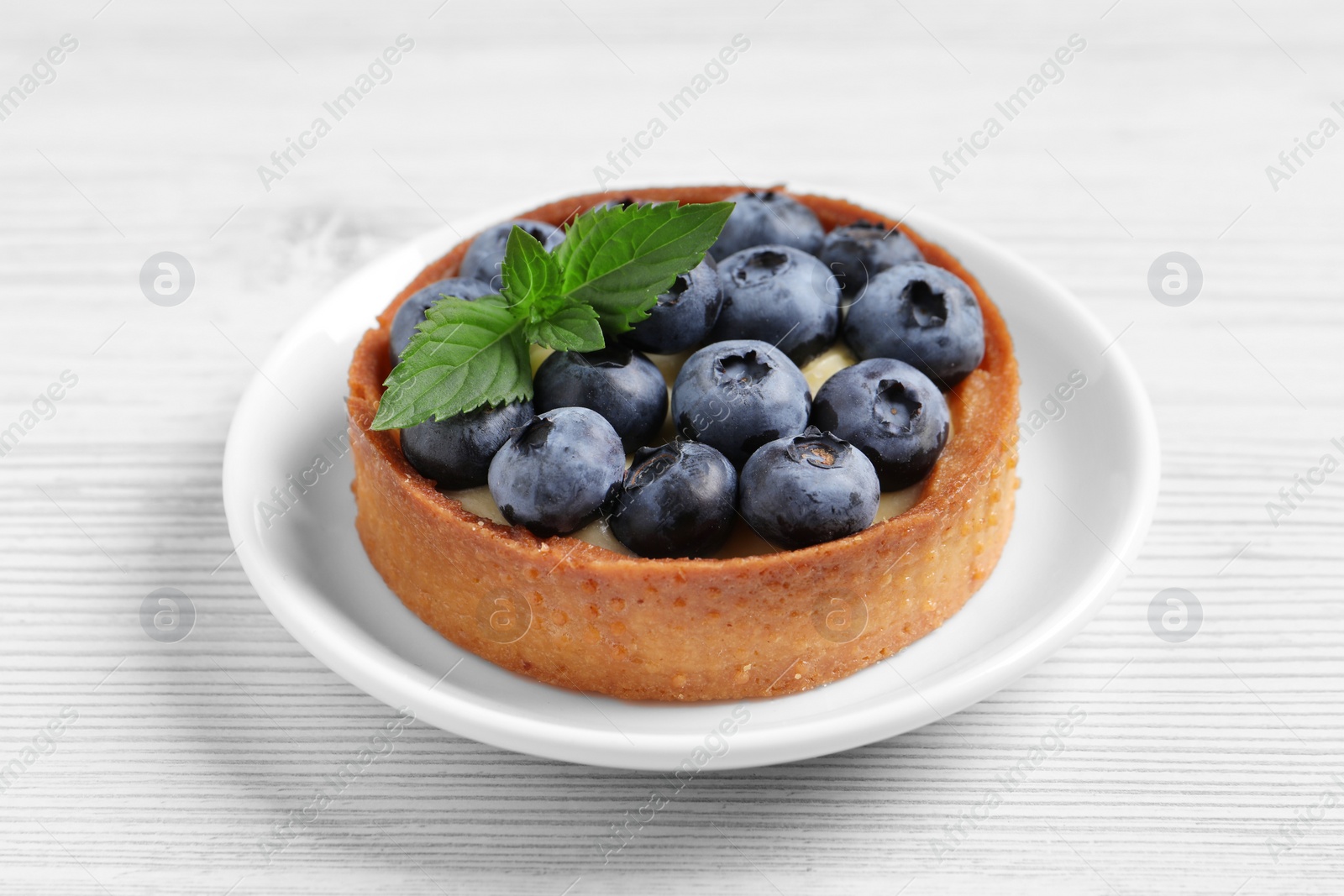 Photo of Tartlet with fresh blueberries on white wooden table, closeup. Delicious dessert