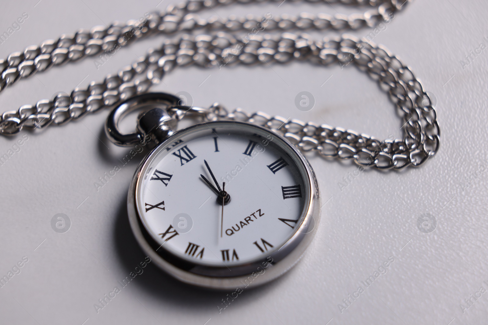 Photo of Silver pocket clock with chain on light table, closeup