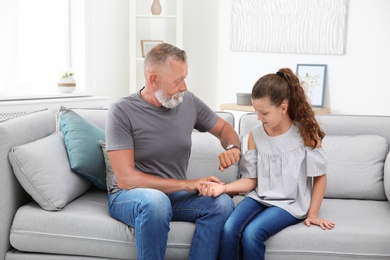 Senior man checking little girl's pulse indoors