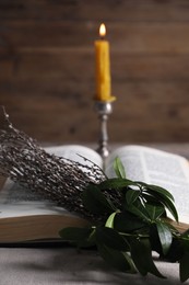 Bible, willow branches and burning candle on table, closeup