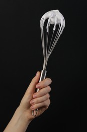 Photo of Woman holding whisk with whipped cream on black background, closeup