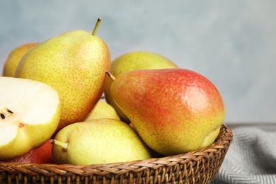 Photo of Wicker basket with ripe juicy pears against blue background, closeup