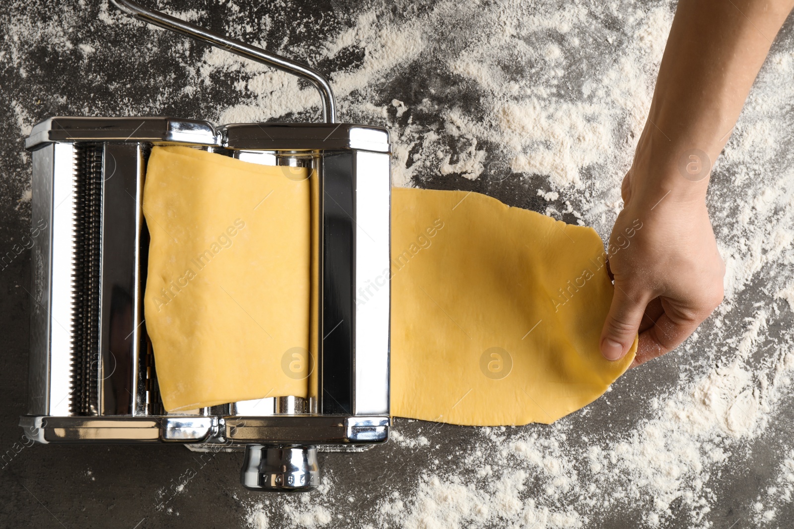 Photo of Woman preparing dough with pasta maker machine at grey table, top view