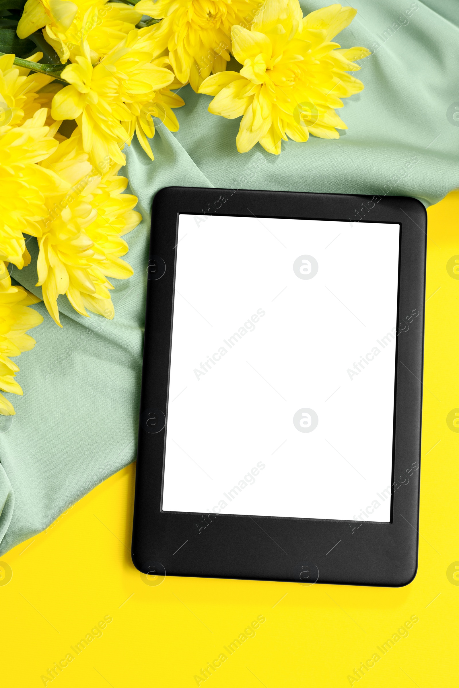 Photo of Modern e-book reader and flowers on yellow background, flat lay