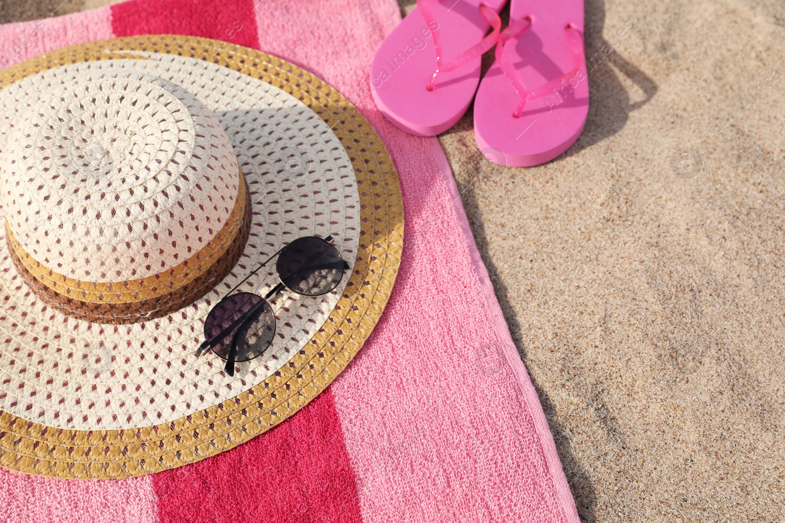Photo of Beach towel with slippers, straw hat and sunglasses on sand