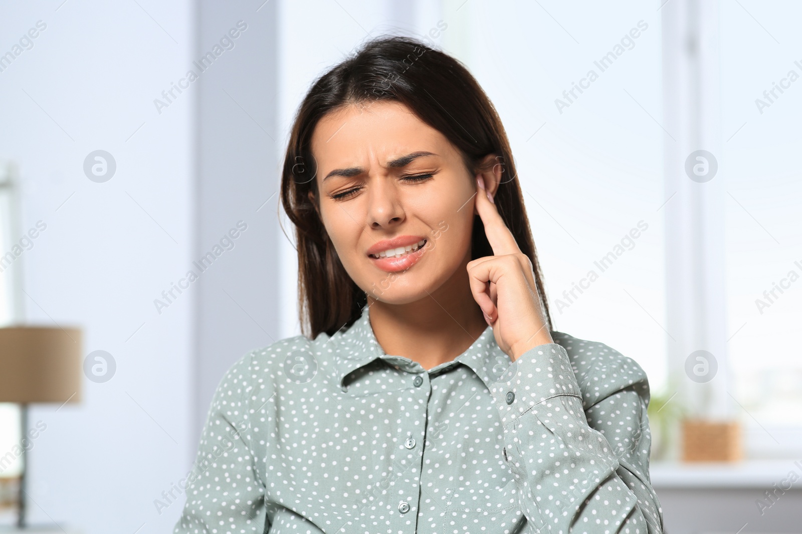 Photo of Young woman suffering from ear pain indoors