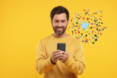 Discount offer. Happy man holding smartphone on yellow background. Confetti and streamers near him