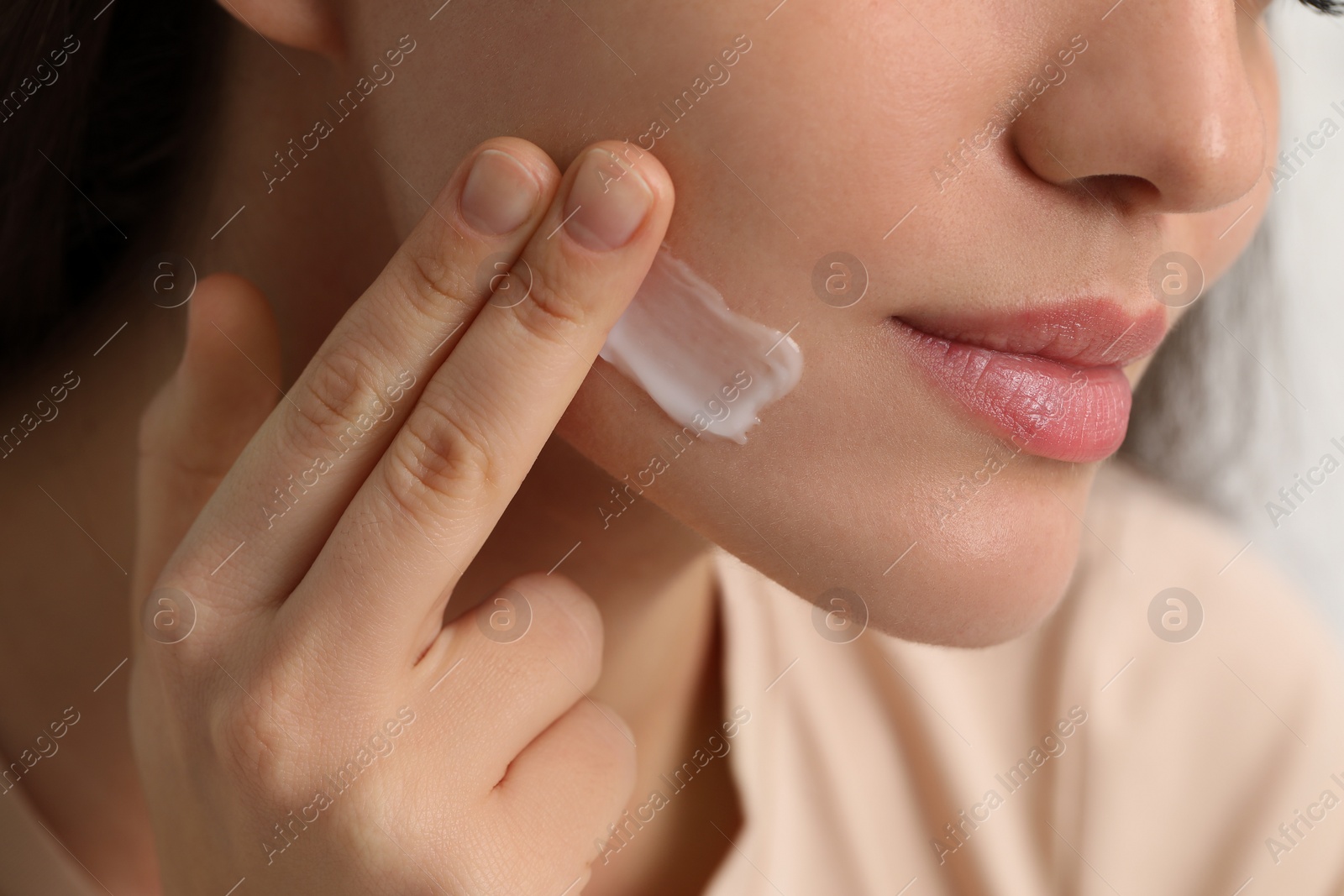 Photo of Young woman with dry skin applying cream onto her face, closeup