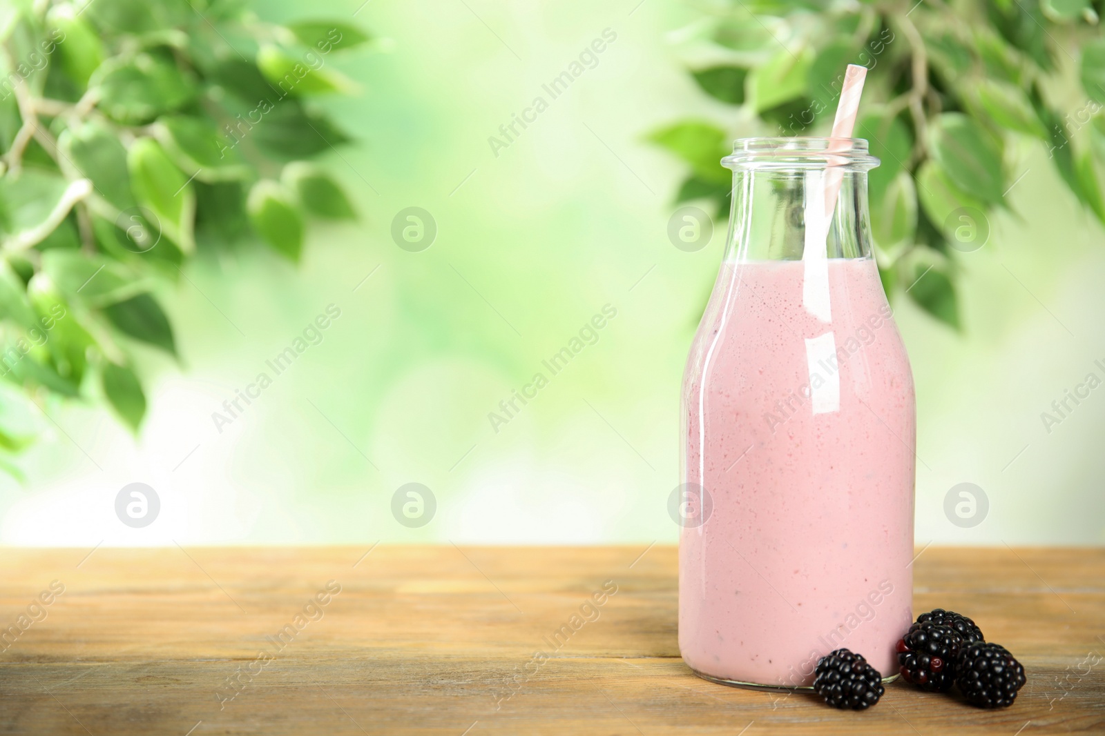 Photo of Tasty fresh milk shake and blackberries on wooden table. Space for text