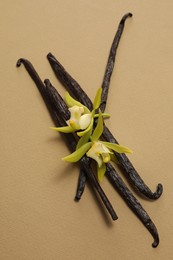 Photo of Vanilla pods and beautiful flowers on dark beige background, top view