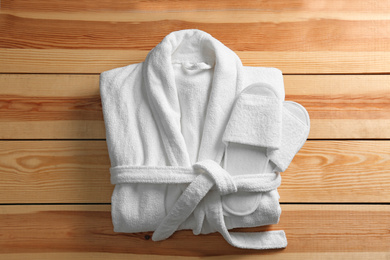 Photo of Clean folded bathrobe and slippers on wooden background, top view