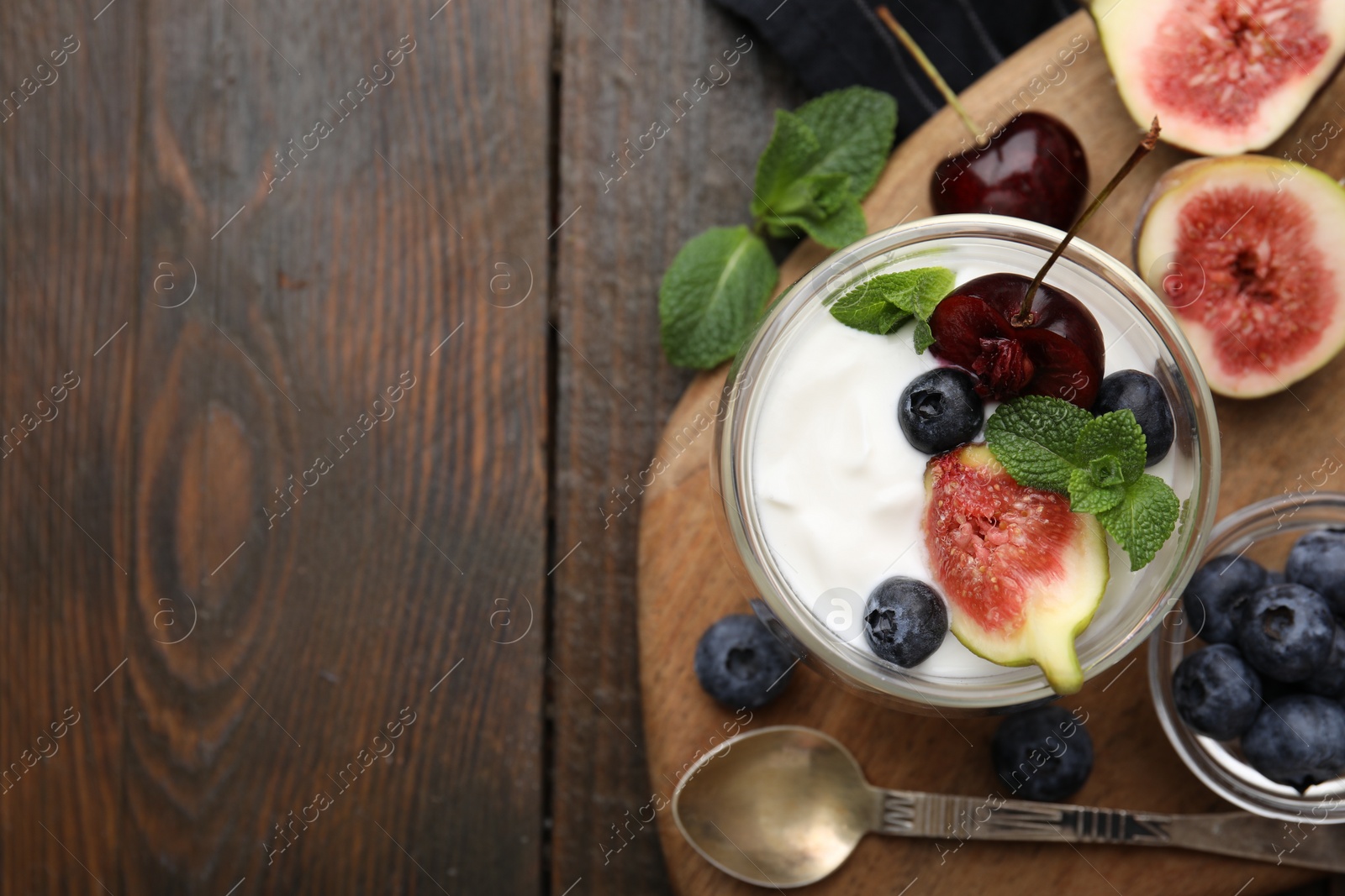 Photo of Glass with yogurt, berries and mint on wooden table, top view. Space for text