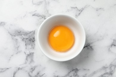 Photo of Bowl with raw egg yolk on white marble table, top view