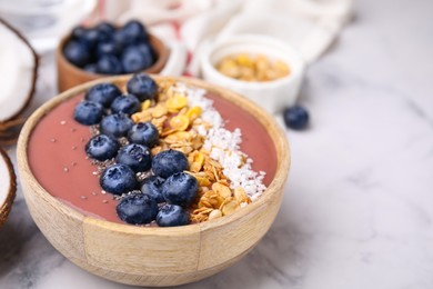 Photo of Bowl of delicious fruit smoothie with fresh blueberries, granola and coconut flakes on white marble table, closeup. Space for text
