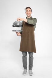 Photo of Handsome waiter holding metal tray with lid on light background