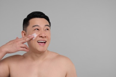 Handsome man applying cream onto his face on light grey background. Space for text