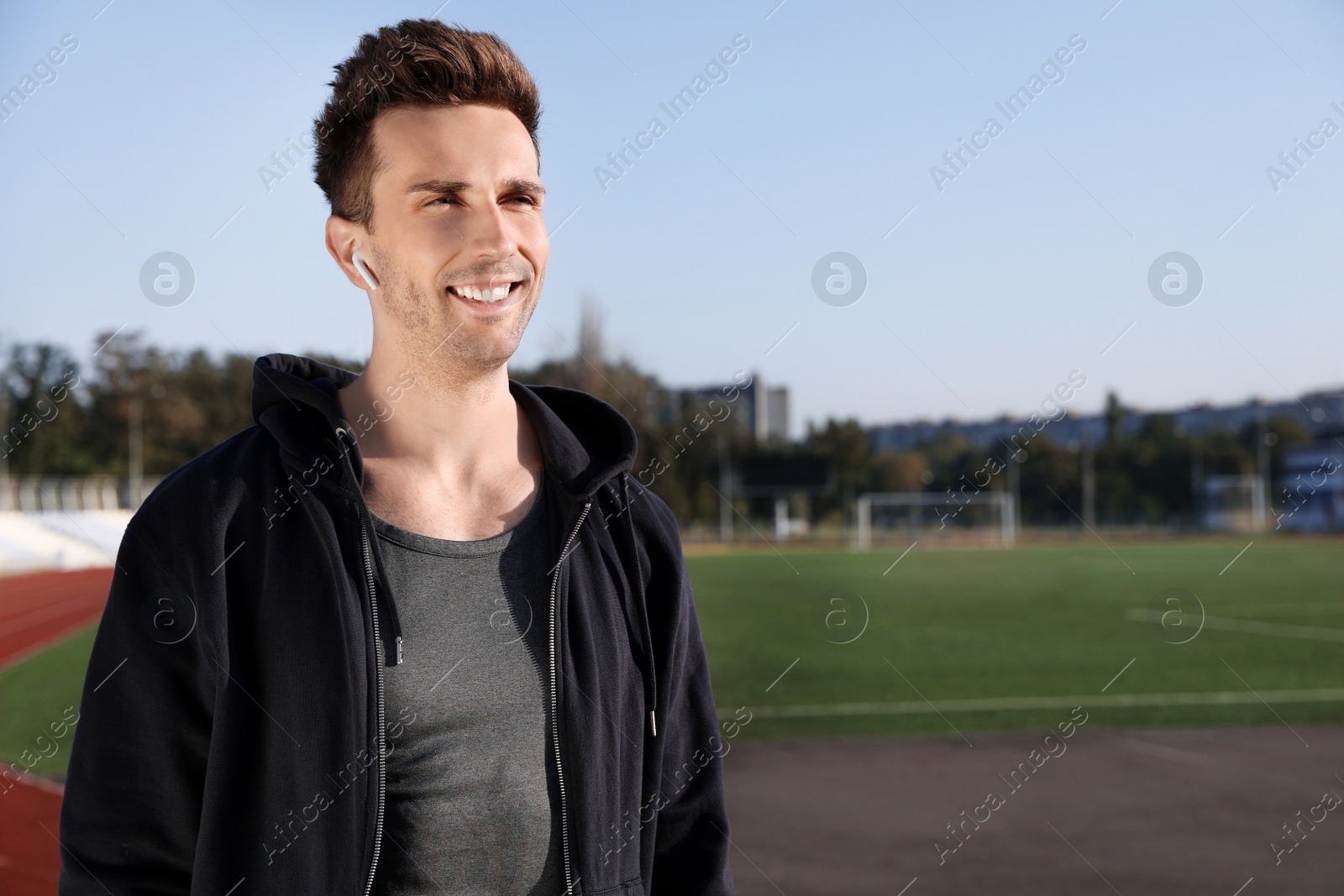 Photo of Young sportsman with wireless earphones at stadium