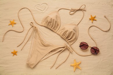 Stylish bikini, sunglasses and starfishes on sand, flat lay