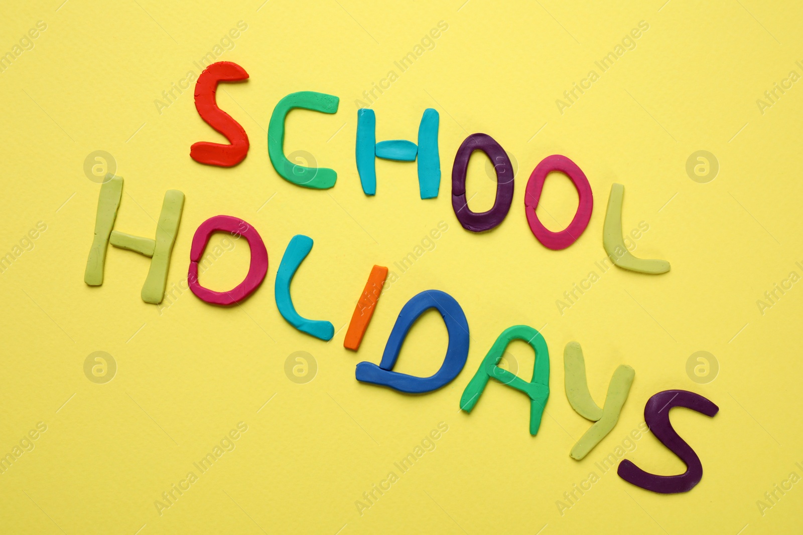 Photo of Phrase School Holidays made of modeling clay on yellow background, top view