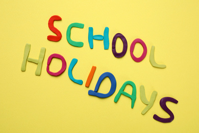 Phrase School Holidays made of modeling clay on yellow background, top view