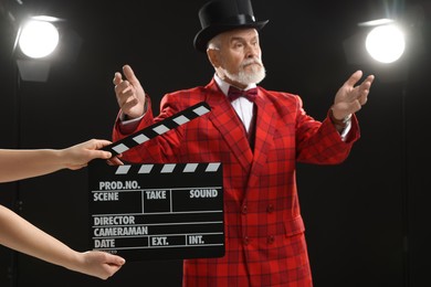 Photo of Senior actor performing role while second assistant camera holding clapperboard on stage, selective focus. Film industry