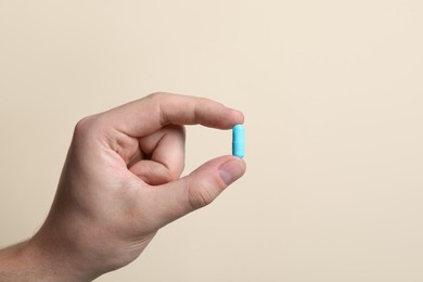 Photo of Man holding pill on beige background, closeup