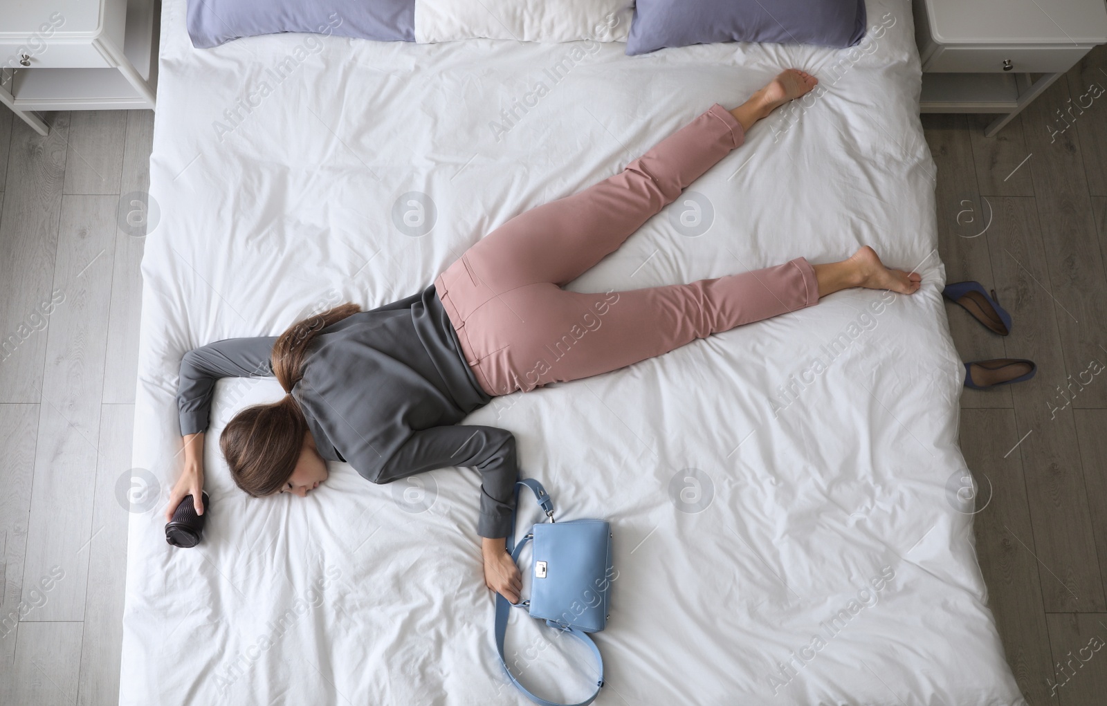 Photo of Exhausted woman with cup of coffee and purse sleeping fully dressed on bed at home, above view