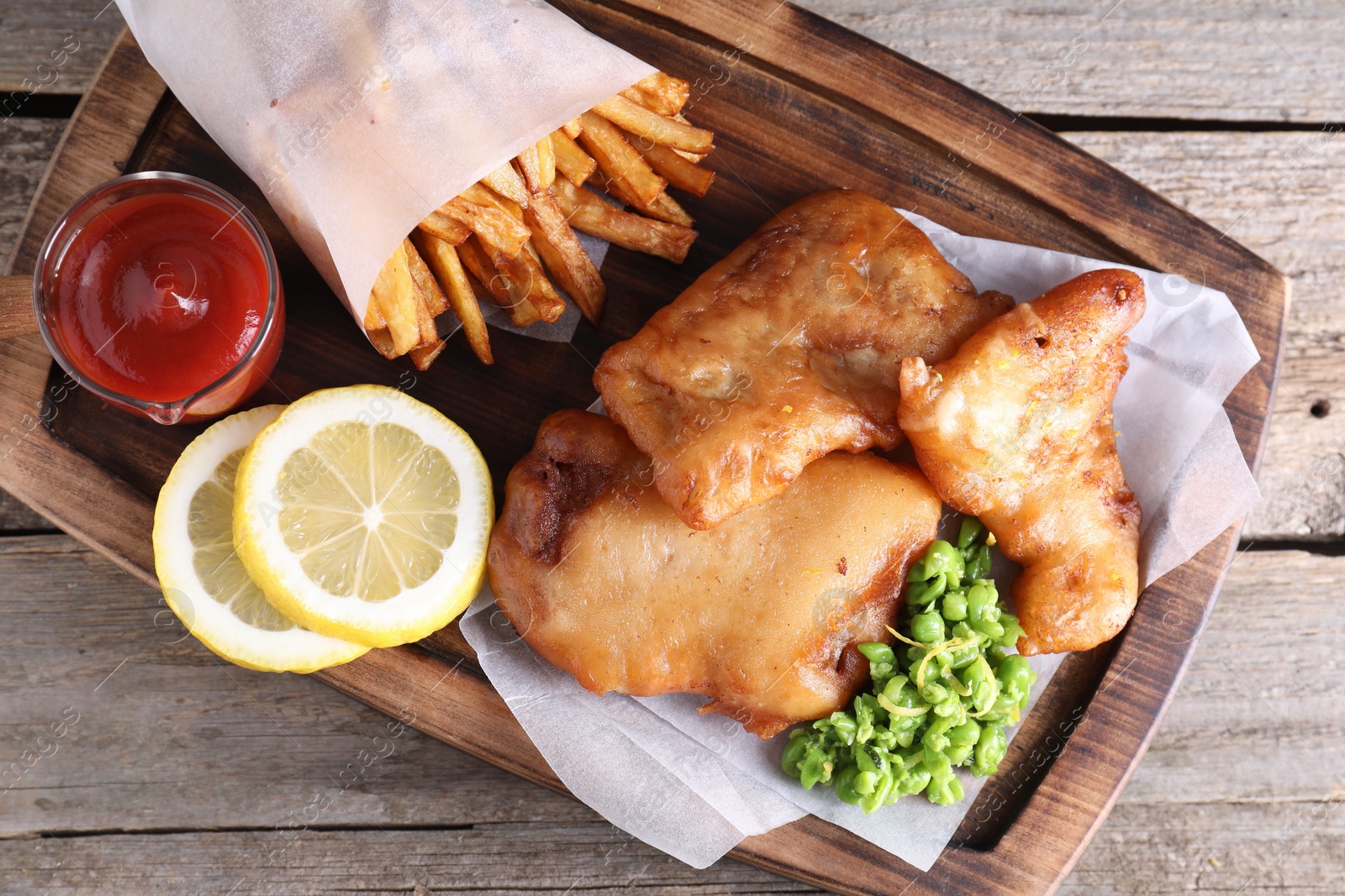 Photo of Tasty fish, chips, sauce and peas on wooden table, top view