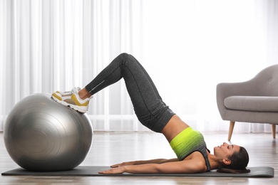 Photo of Young woman doing exercise with fitness ball at home