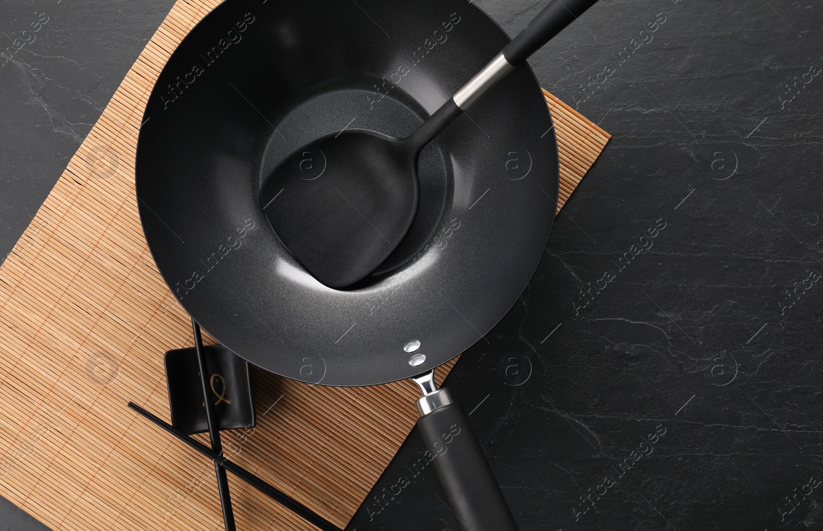 Photo of Black metal wok, chopsticks and spatula on dark textured table, top view