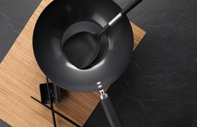 Black metal wok, chopsticks and spatula on dark textured table, top view