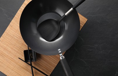 Photo of Black metal wok, chopsticks and spatula on dark textured table, top view