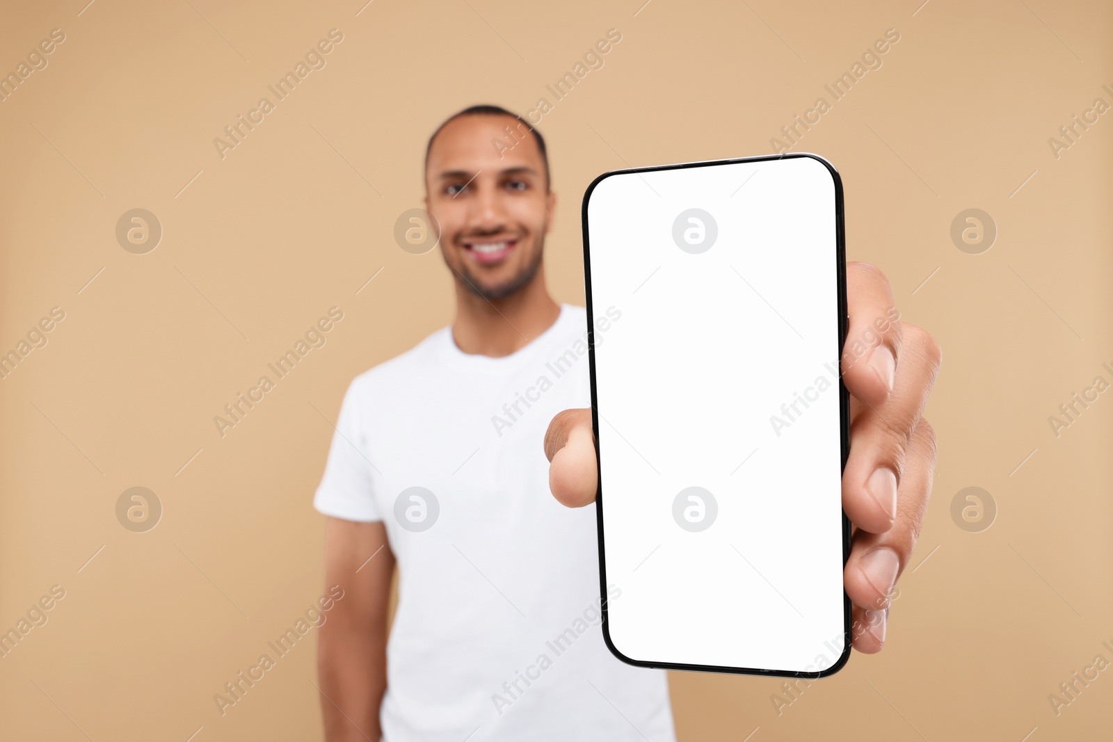 Photo of Young man showing smartphone in hand on beige background, selective focus. Mockup for design