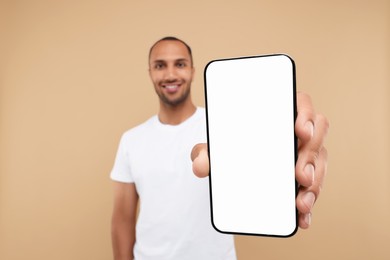 Photo of Young man showing smartphone in hand on beige background, selective focus. Mockup for design