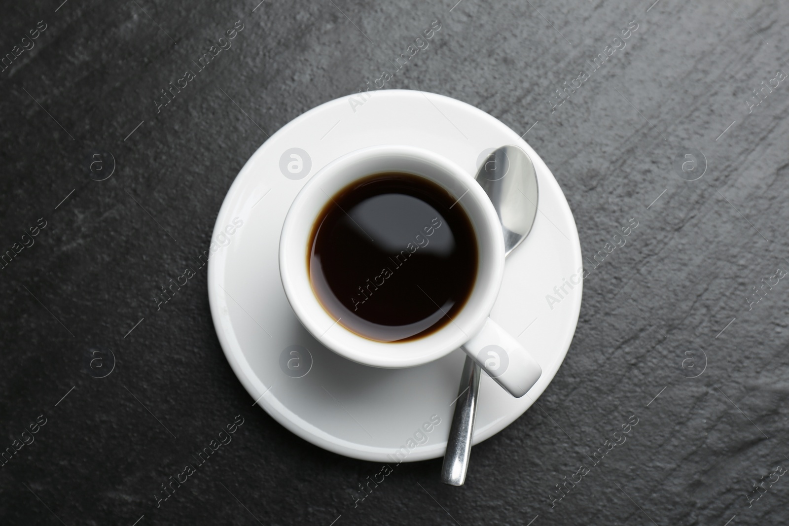 Photo of Hot coffee in cup, spoon and saucer on dark textured table, top view