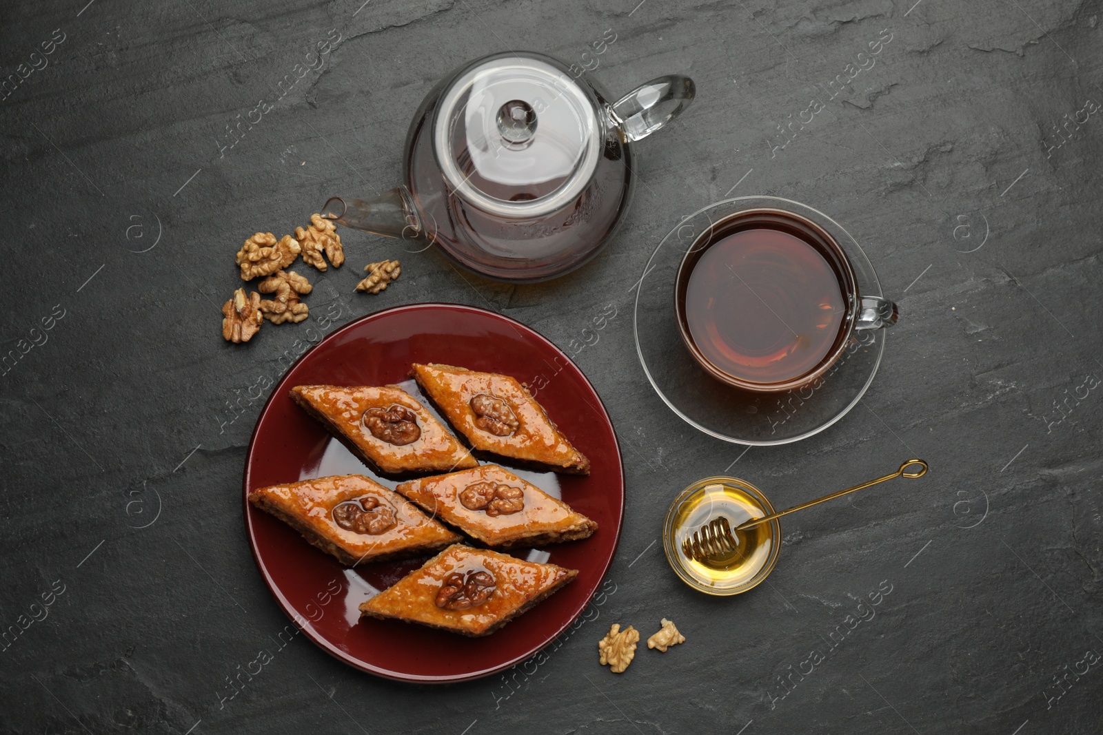 Photo of Delicious sweet baklava with walnuts, honey and hot tea on black table, flat lay