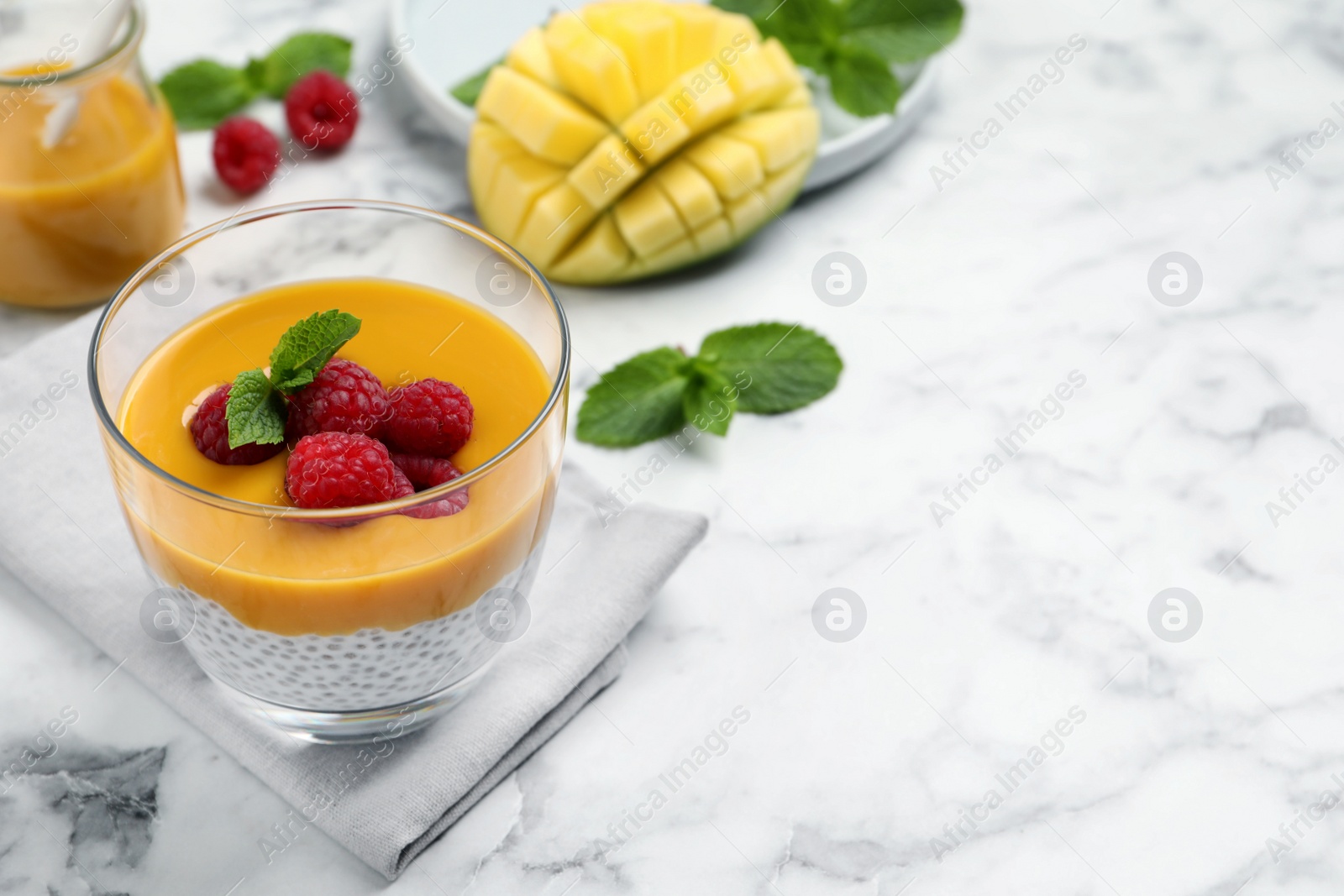 Photo of Delicious chia pudding with mango sauce and raspberries on white marble table. Space for text