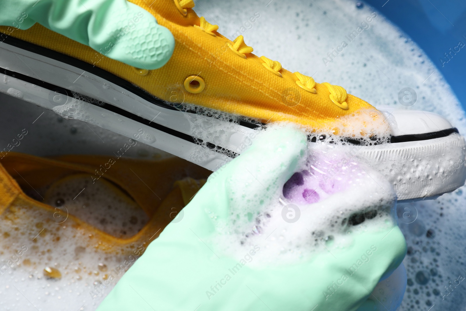 Photo of Woman with gloves and sponge cleaning stylish sneakers in wash basin, top view