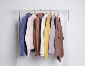Warm sweaters hanging on rack against white background
