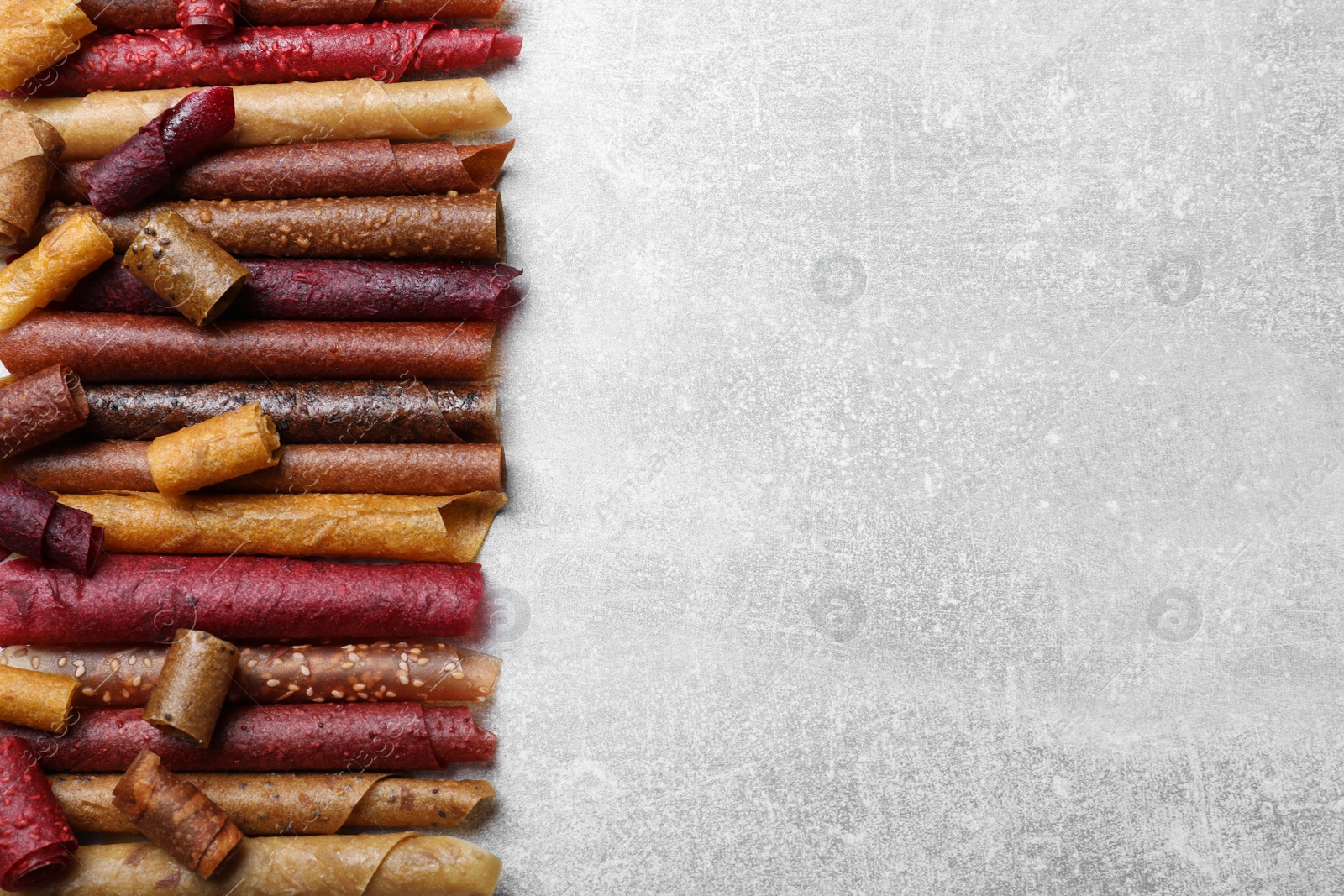 Photo of Delicious fruit leather rolls on grey table, flat lay. Space for text