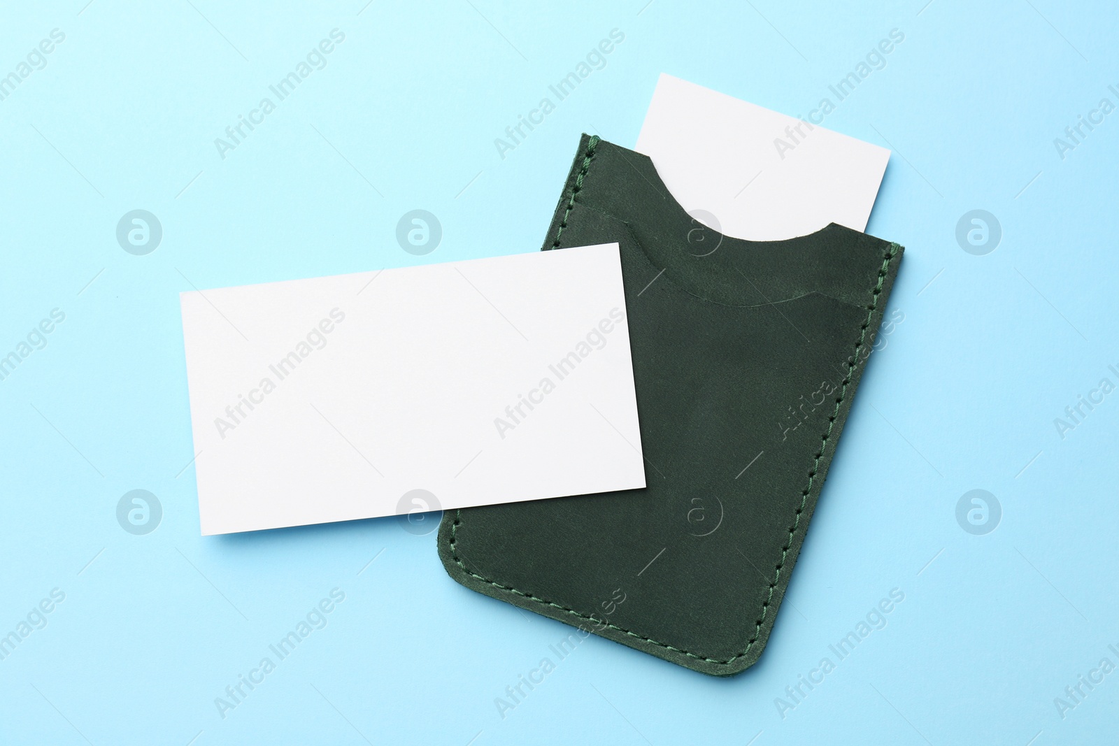 Photo of Leather business card holder with blank cards on light blue background, top view