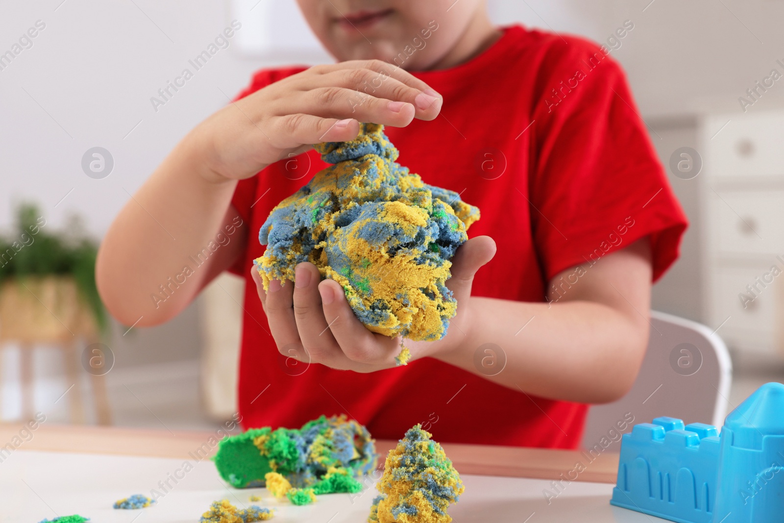 Photo of Little boy playing with bright kinetic sand at table in room, closeup